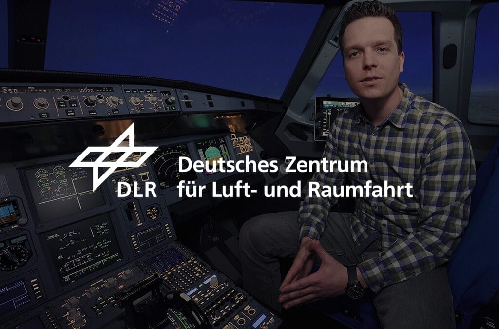 Mann sitzt im Cockpit eines Flugzeugs und schaut in die Kamera, während er vor Steuerungselementen steht.