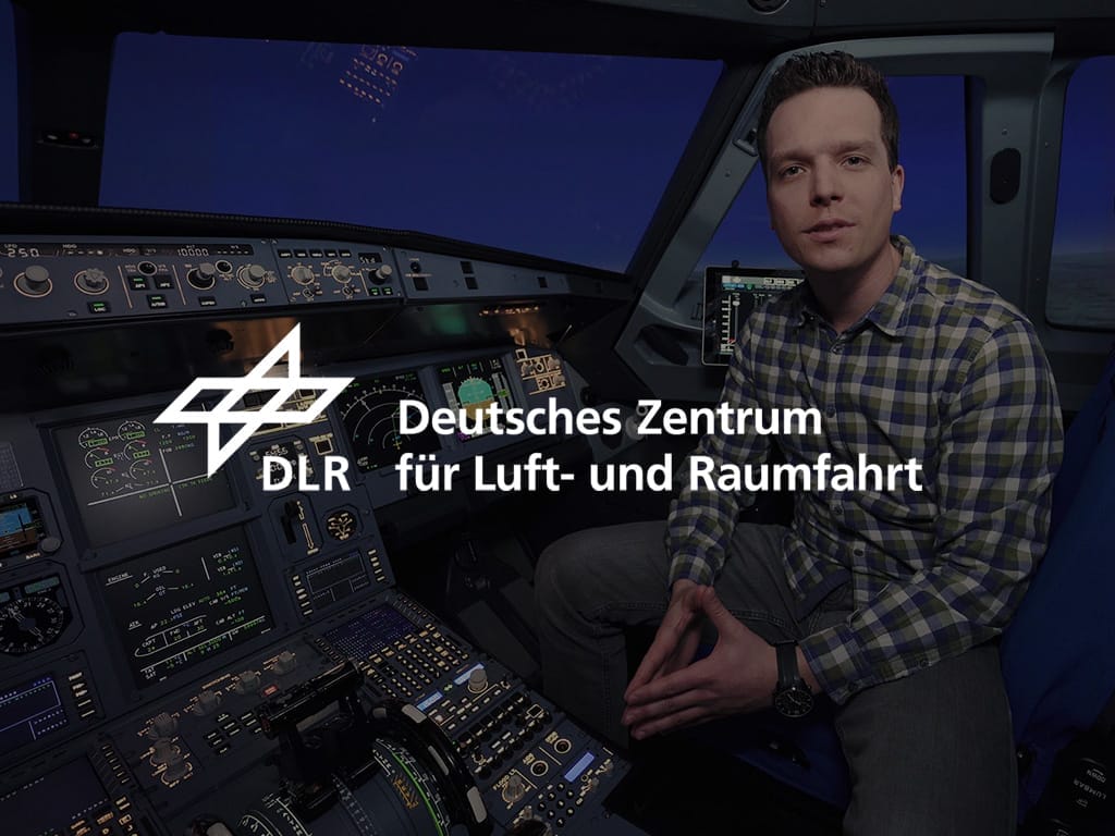 Mann sitzt im Cockpit eines Flugzeugs und schaut in die Kamera, während er vor Steuerungselementen steht.