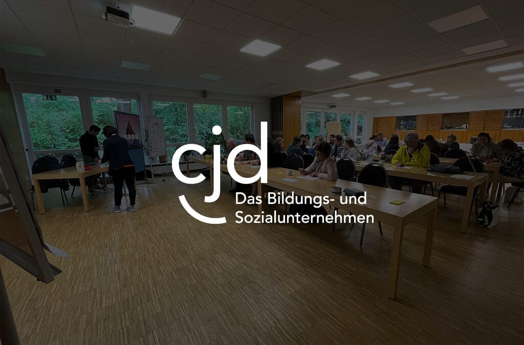 Teilnehmer bei einer Veranstaltung des CJD Bildungs- und Sozialunternehmens in einem Raum mit Tischen und Stühlen.