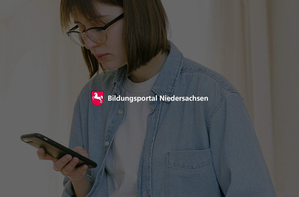 Junge Frau mit Brille, die auf ihr Smartphone schaut, trägt eine blaue Jeansjacke.