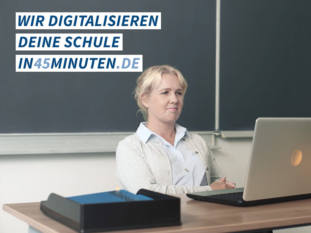 Frau sitzt an einem Schreibtisch mit einem Laptop und schaut nachdenklich in die Kamera.