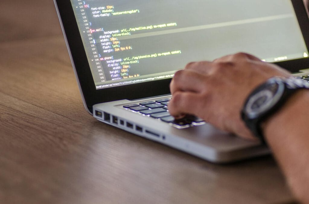 Eine Hand tippt auf die Tastatur eines Laptops, während Code auf dem Bildschirm angezeigt wird.