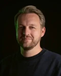 Porträt eines Mannes mit blonden Haaren und Bart, der in die Kamera lächelt.