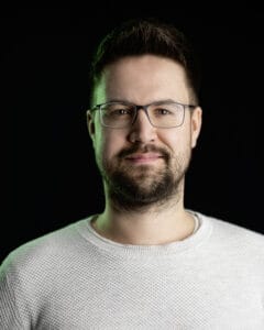 Porträt eines Mannes mit Brille und Bart, der in die Kamera lächelt.