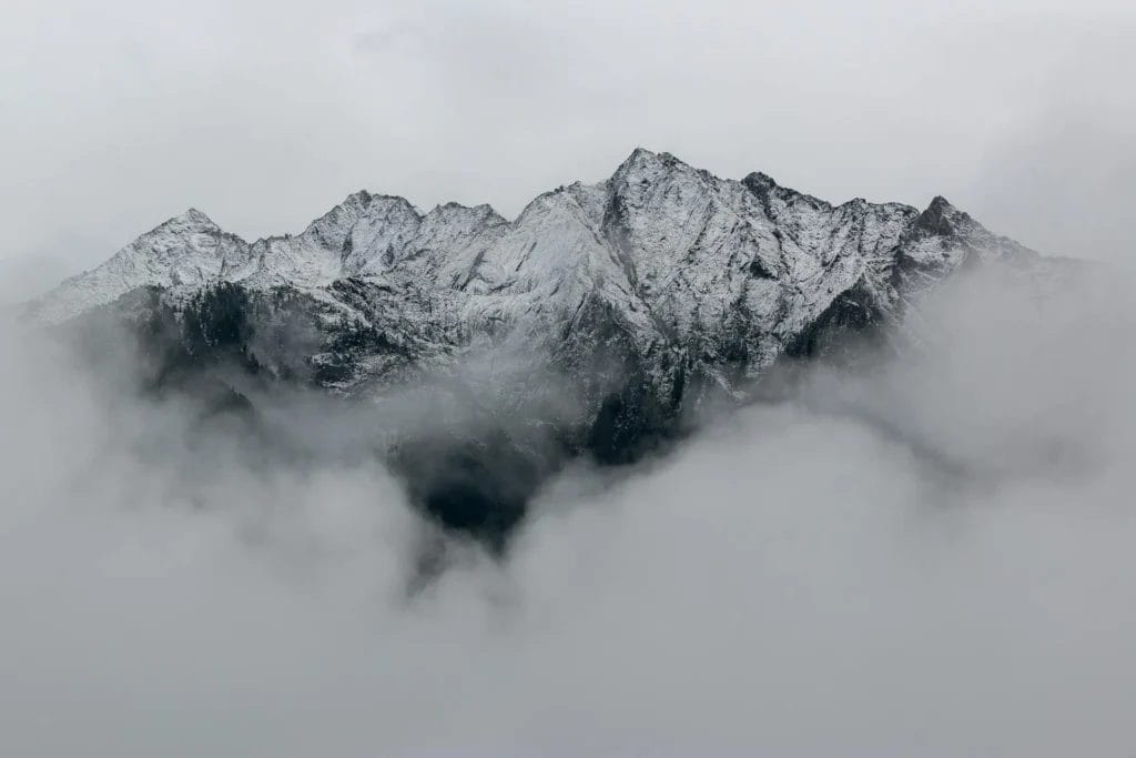 Schneebedeckte Bergspitze, die aus einer Wolkendecke herausragt, mit grauem Himmel im Hintergrund.
