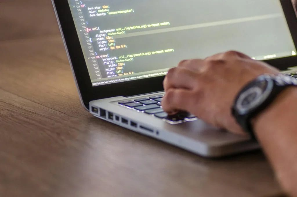 Nahaufnahme einer Hand, die auf der Tastatur eines Laptops tippt, während Programmiercode auf dem Bildschirm angezeigt wird.