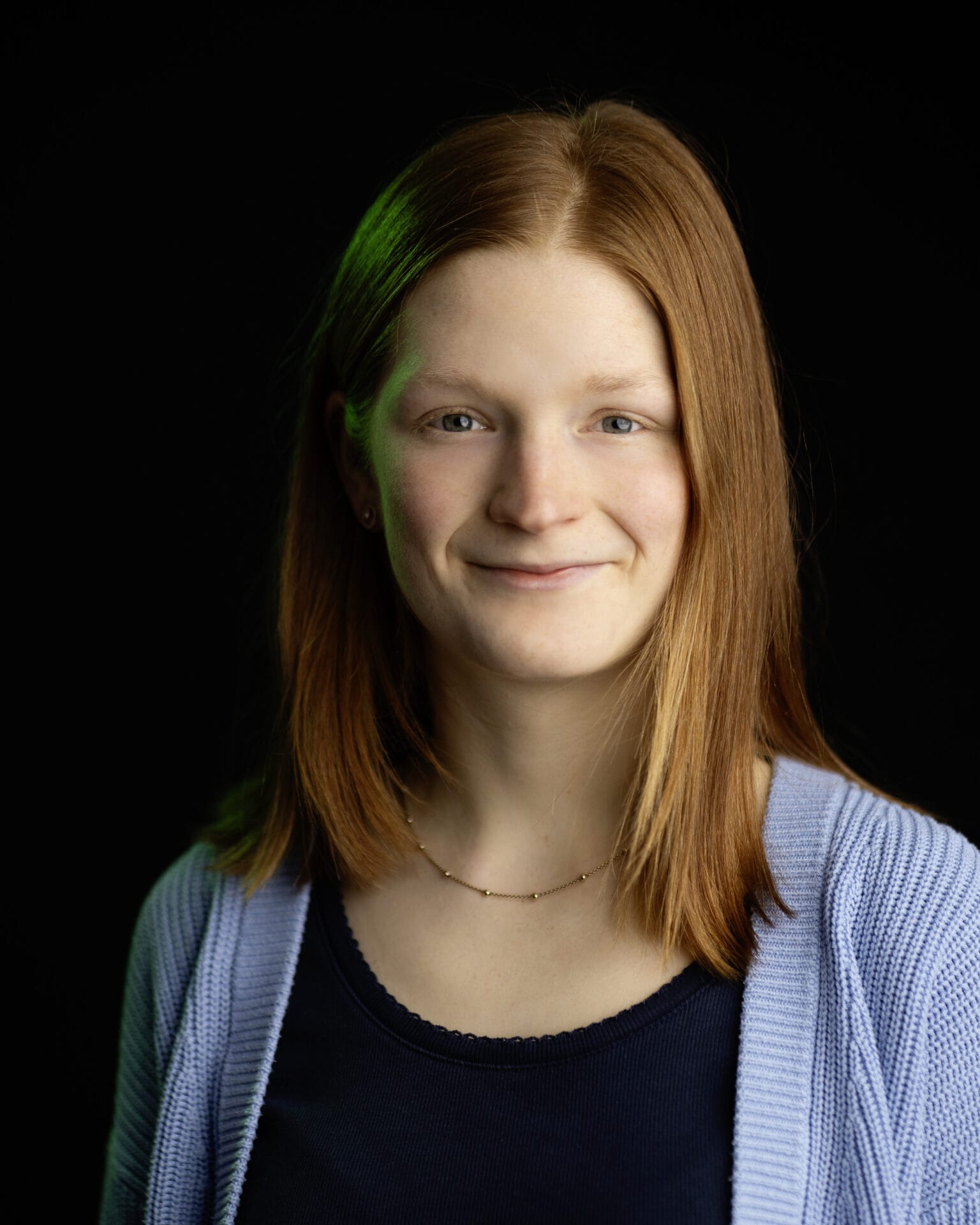 Porträt einer Frau mit schulterlangen, roten Haaren vor dunklem Hintergrund in Studioaufnahme.